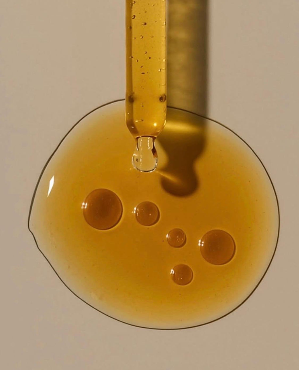 A drop of LILVAA rosehip oil falling from the dropper into a golden pool